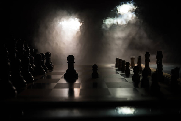 Juego de mesa de ajedrez concepto de ideas de negocio y competencia. Figuras de ajedrez sobre un fondo oscuro con humo y niebla
. - Foto, Imagen