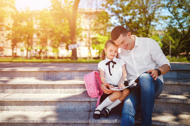 Father and little daughter sitting on stairs and read book, study lessons. Parenthood and child concept - Photo, image