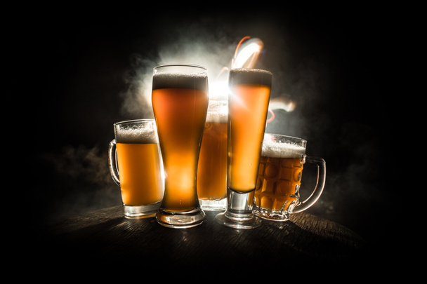 Creative concept. Beer glasses on wooden table at dark toned foggy background. - 写真・画像