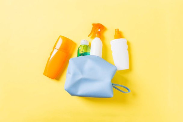 Top view of female cosmetics bag full of suncream spray, sunsreen, sunblock and body lotion and spf cream on yellow background with copy space. Directly above. Bright summer concept - Photo, Image