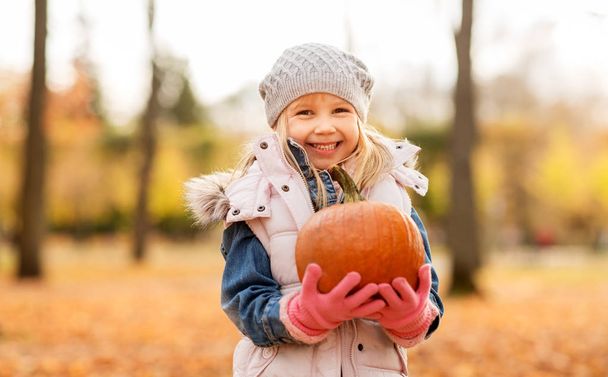 happy little girl with pumpkin at autumn park - Foto, afbeelding