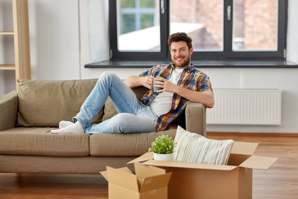 man with boxes and drinking coffee at new home - Photo, image