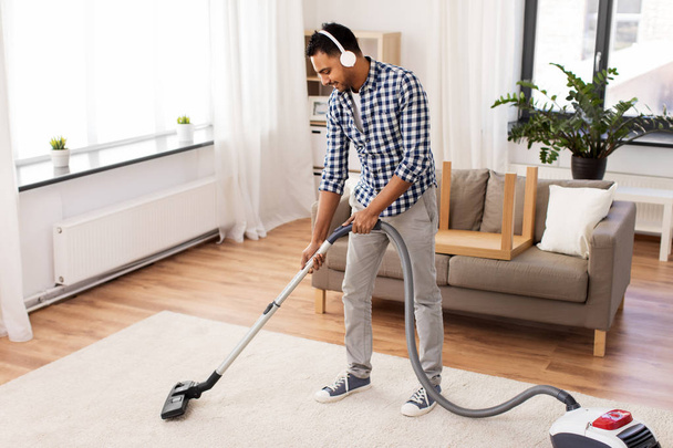 man in headphones with vacuum cleaner at home - Zdjęcie, obraz