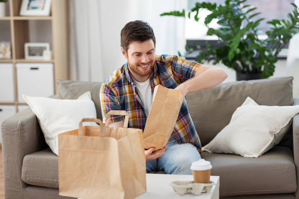 smiling man unpacking takeaway food at home - Foto, afbeelding