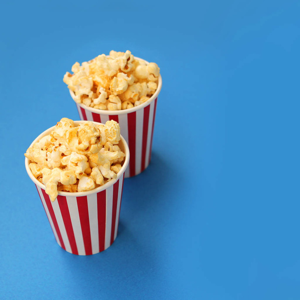 two striped white and red paper cups with fragrant crispy popcorn stand one after another on a light blue background, copy space, close-up, square - Photo, image