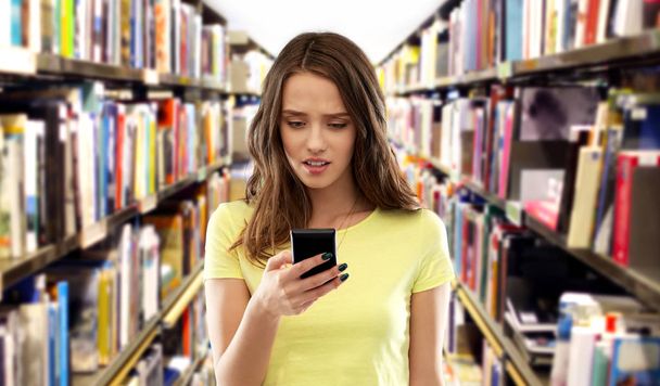 adolescente estudiante utilizando smartphone en la biblioteca - Foto, Imagen