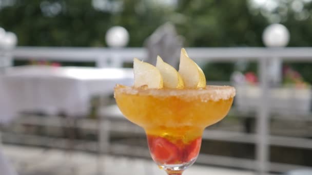 Fresh summer cocktail concept. Berries and ice cubes splash falling down into gluss with beautifully decorated fruit cocktail , shot in slow motion on blurred restaurant open summer terrace. Food - Πλάνα, βίντεο
