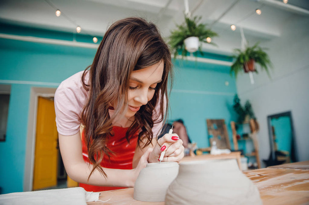 Work potter wheel. Happy young woman in red apron sculpts from clay - Photo, Image