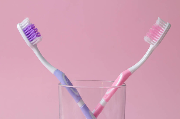 Higiene oral. cepillo de dientes multicolor en un vaso sobre un fondo rosa brillante
. - Foto, Imagen
