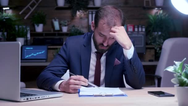 Nagyítás lövés fáradt és kimerült üzletember dolgozik késő este az irodában - Felvétel, videó