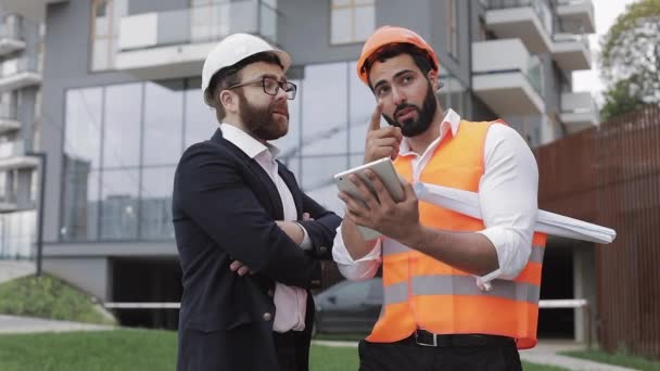 Construction manager and architect man are discussing the construction plan of the modern business center. They checks the work with a tablet. Outside. - Materiał filmowy, wideo