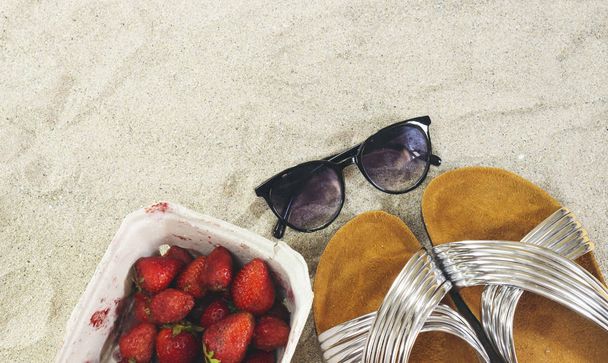Γυαλιά ηλίου και παντόφλες και κουτί φράουλας στην άμμο, καλοκαιρινή ιδέα - Φωτογραφία, εικόνα