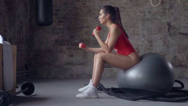 Ελκυστικό κορίτσι κάνει άσκηση με κόκκινα βαράκια στο φόντο ενός τοίχου τούβλο - Πλάνα, βίντεο