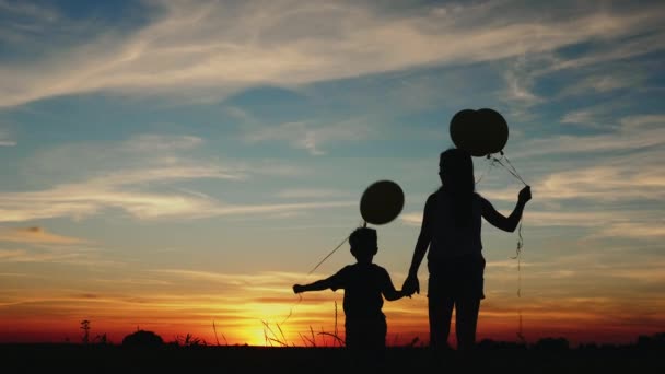 Silhouet twee kinderen met ballonnen bij zonsondergang - Video