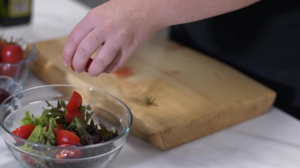A female hand cuts cherry tomato for her healthy salad - Imágenes, Vídeo
