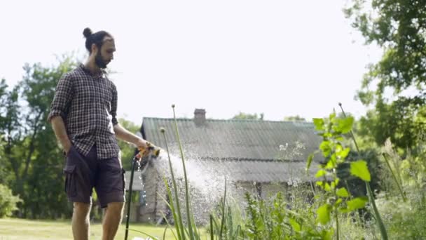 Young handsome hipster man watering the garden with a garden hose.  - Video