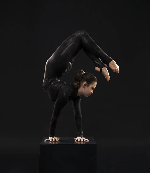 黒いスーツを着た魅力的な女の子の体操選手は、逆の光の中でアクロバットに従事. - 写真・画像