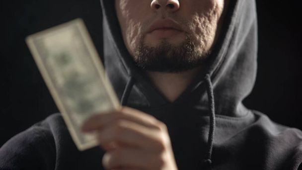 Dangerous gangster holding money in dark room full of smoke, payment for crime - Foto, imagen