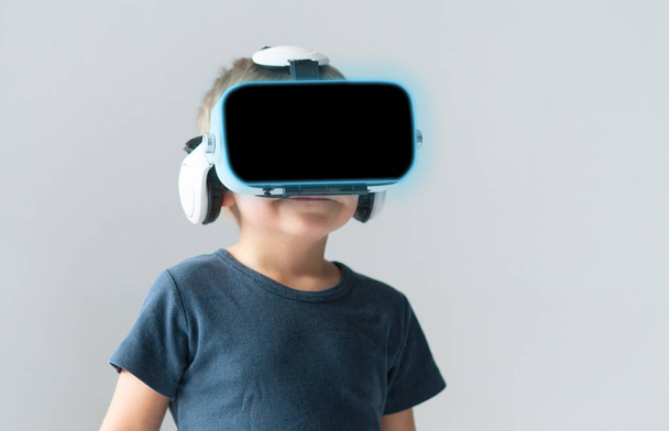 Portrait of happy kid in a virtual reality headset. Attractive kid using vr goggles over abstract background. Entertainment technology, futuristic gadgets and generation Z concept. - Fotoğraf, Görsel