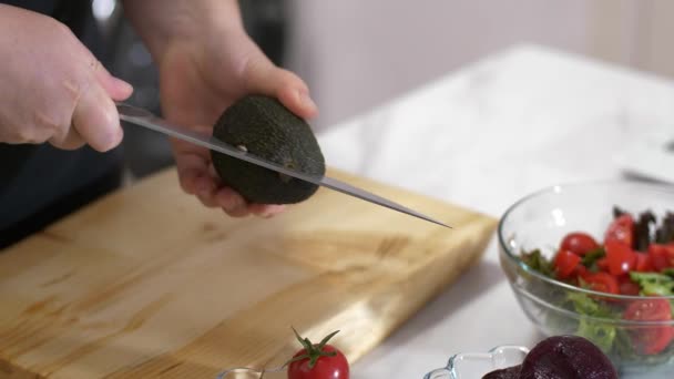 A female hand cuts avocado o for her healthy salad - Πλάνα, βίντεο