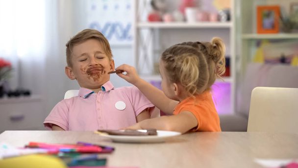Girl feeding smeared boy with chocolate, sweets overeating, stomach problems - Photo, image