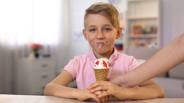 Boy tasting ice-cream cone from female hand sitting at table, childhood dessert - Zdjęcie, obraz