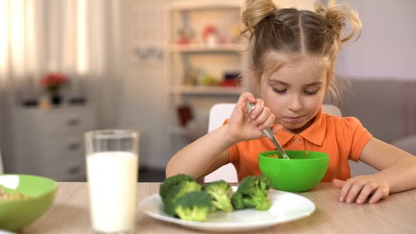 Ongelukkig meisje eten gezond maar smakeloos eten, broccoli liggen op tafel, dieet - Foto, afbeelding