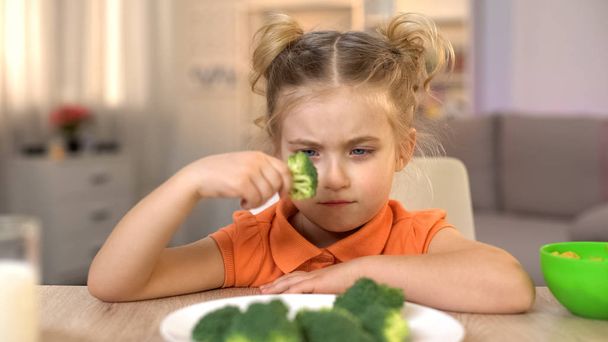 Upset girl looking at broccoli with disgust, full of vitamins but tasteless food - Фото, зображення