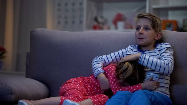 Brother hugging scared sister while watching horror film together night, family - Fotoğraf, Görsel
