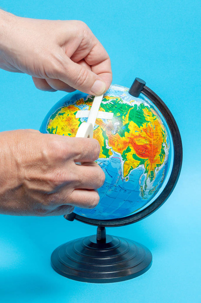 Male hand putting a patch on a globe. Geographical names on the globe in Russian - 写真・画像