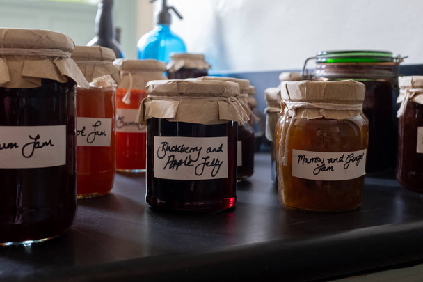 mehrere Gläser hausgemachte Marmelade auf einer Arbeitsplatte sitzend, mit altmodischem braunem Papier und Saitendeckeln mit handgeschriebenen Etiketten - Foto, Bild