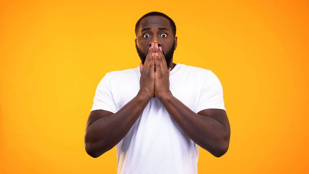 Young surprised black man closing his mouth with hands on yellow background - Φωτογραφία, εικόνα