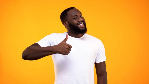 Young bearded black guy showing thumbs up, smiling on camera yellow background - Φωτογραφία, εικόνα