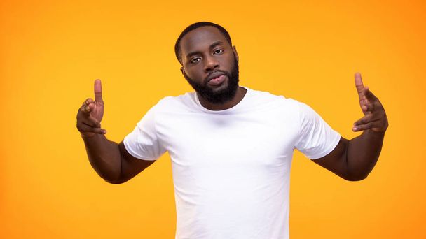 Angry black male pointing finger guns on camera on yellow background, aggression - Foto, imagen