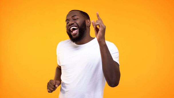 Happy relaxed black man dancing against yellow background, having fun on party - Photo, image