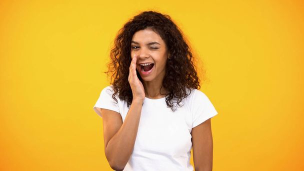Smiling woman whispering secrets and winking on camera yellow background, rumors - Foto, imagen