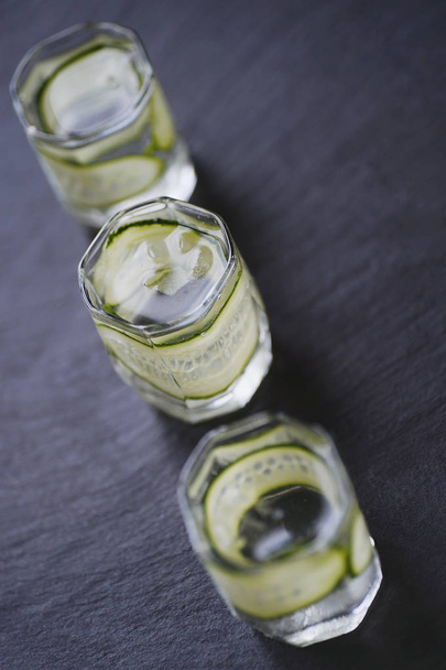 Vodka in shot glasses with cucomber on rustic wood backgroun - 写真・画像