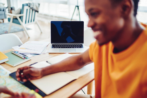Selective focus on modern laptop computer for learning on desktop, smiling african american male student on blurred frontage satisfied with studying process using modern technologies and wif - 写真・画像