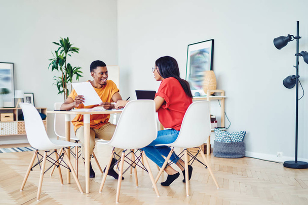 Mosolygó sötét bőrű férfi és női kollégák beszélgetnek egymással elégedett együttműködés, vidám afro-amerikai diákok tanulnak együtt fényes lakás modern bútorokkal - Fotó, kép