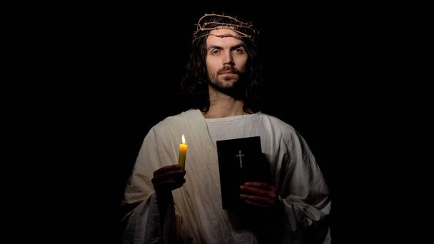 Saint in crown of thorns holding candle and holy bible, christian faith in god - 写真・画像