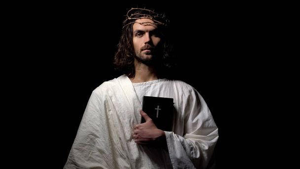 Man in crown of thorns holding bible looking directly, Jesus before crucifixion - Фото, изображение