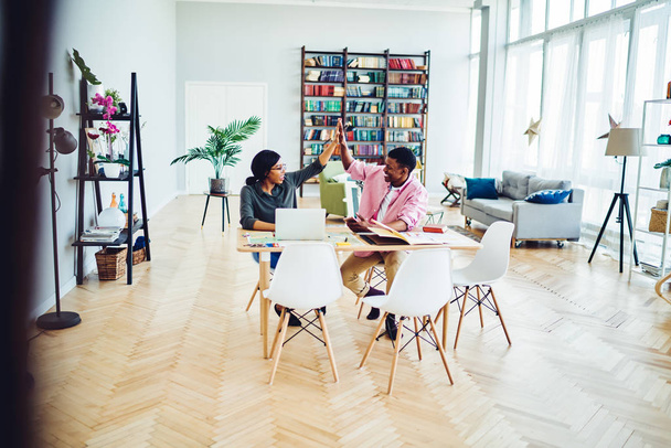 Cheerful male and female dark skinned colleagues satisfied with completed project sitting at desktop, smiling african american couple happy about making successful plan giving high five at hom - Photo, image