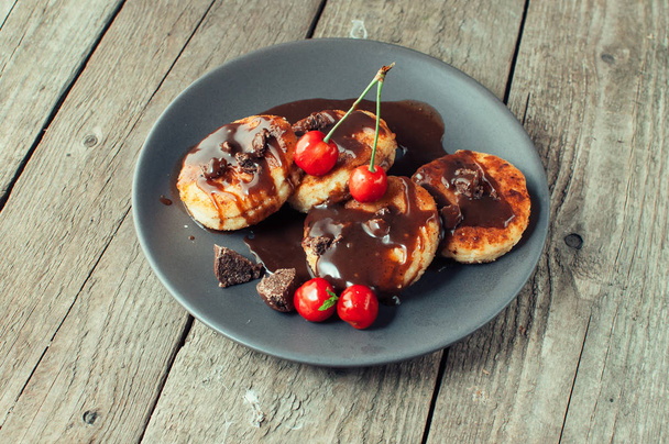 Gourmet breakfast - cottage cheese pancakes, cheese cakes, cottage cheese pancakes with cherries and chocolate in a brown plate. Useful dessert on a wooden table in rustic style. Selective focus. - Foto, Imagen