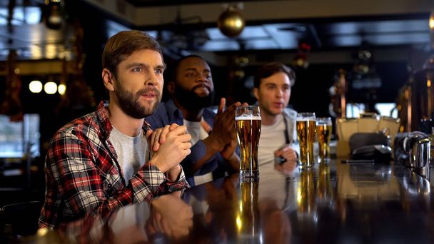 Anxious multiracial friends cheering for sports game in pub, watching game on tv - 写真・画像
