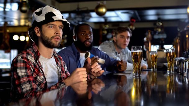 Anxious multiracial male friends watching match in bar, cheering for team goal - Фото, изображение