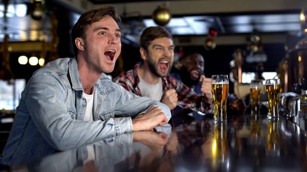 Emotional male fans cheering for favorite team in pub, celebrating game victory - Photo, Image