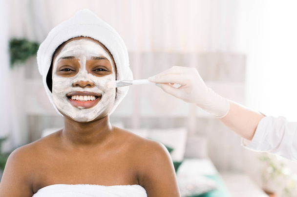 Young African woman in Studio doing body care with refreshing facial mask for young and beautiful skin and relaxation - Foto, Bild