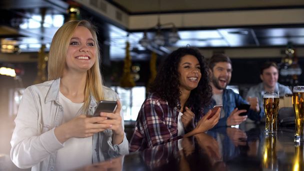 Smiling group of friends in bar celebrating win in sports betting, mobile app - Fotó, kép