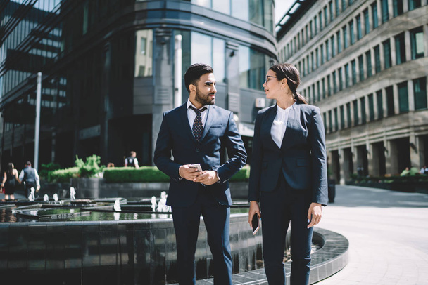 Multicultural male and female entrepreneurs walking around city street in downtown and communicate about upcoming startup project,diverse business people in formal suit strolling in financial district - Fotó, kép