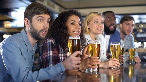 Sport fans holding beer glasses attentively watching sport competition in pub - Foto, Bild
